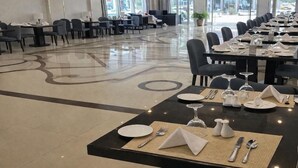 A hotel dining area with tables set for service, a chandelier, and a view of the street through large windows. - Carawan Al Khaleej Hotel Olaya (Riyadh)