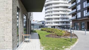 A modern building with a brick facade, a circular balcony structure, and a paved outdoor area with a bench and greenery.