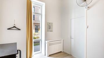 A room with a radiator, a door, a hanging coat rack, and a window with curtains.