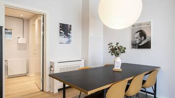 A modern dining area with a dark table, beige chairs, a hanging light fixture, and two framed pictures on the wall.