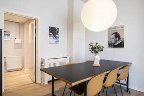 A modern dining area with a dark table, beige chairs, a hanging light fixture, and two framed pictures on the wall. - Flat in Amager with gym sauna (København)