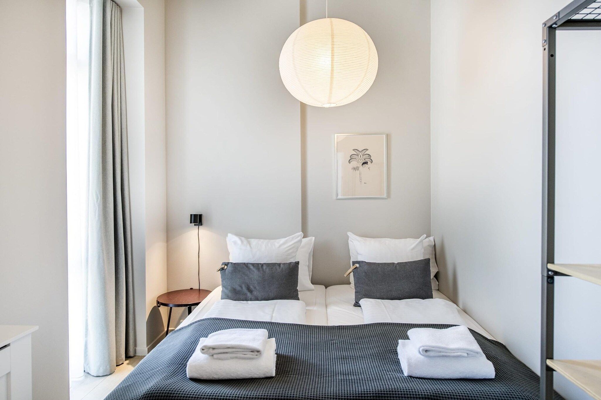 A hotel room with a bed, bedside tables, a hanging light fixture, and a wall-mounted picture.