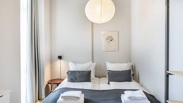 A hotel room with a bed, bedside tables, a hanging light fixture, and a wall-mounted picture.
