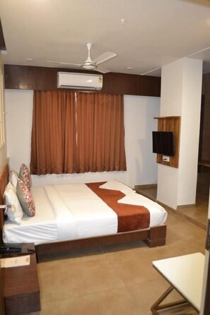 A hotel room with a bed, a TV, an air conditioner, and a ceiling fan.