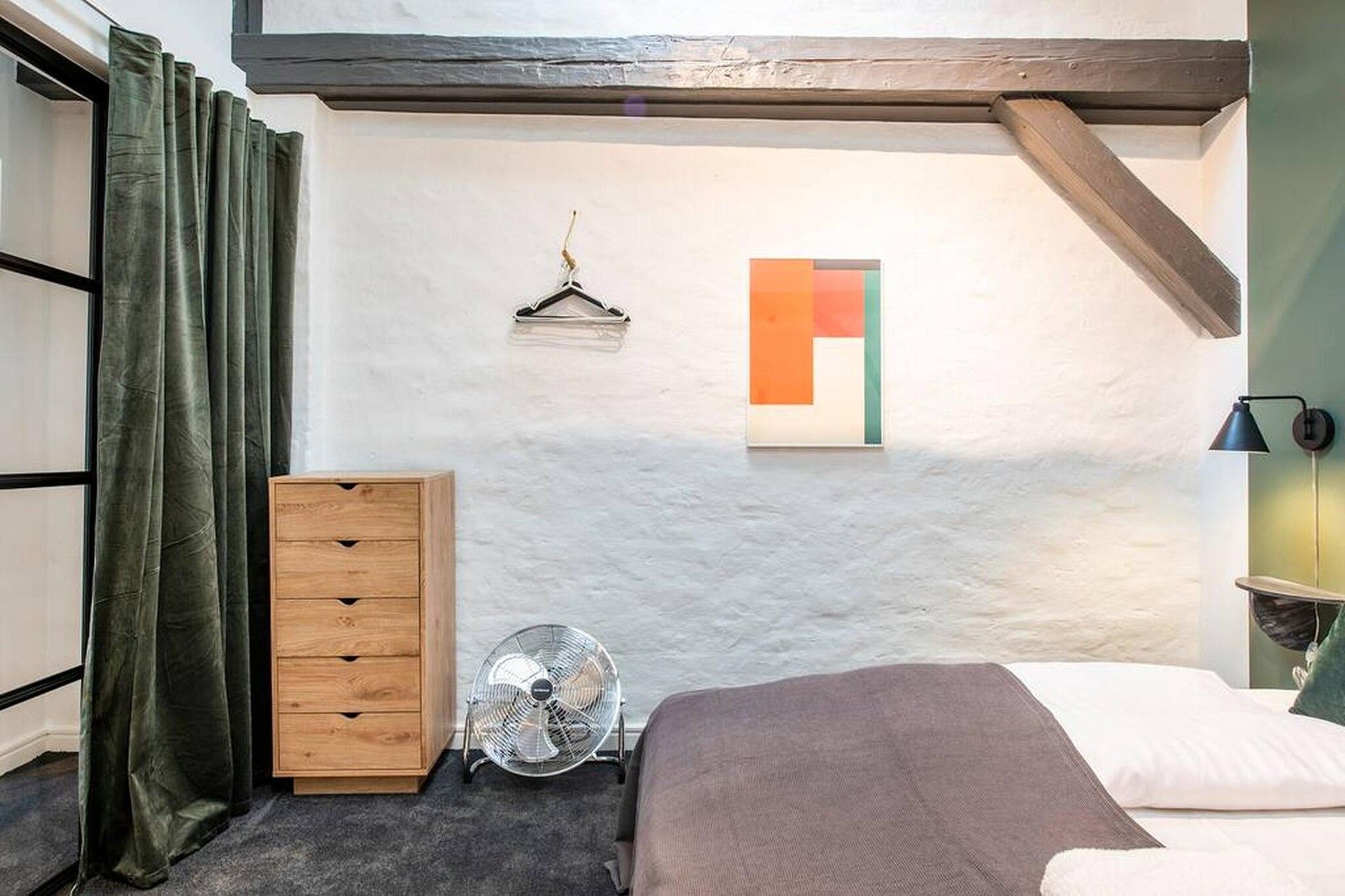 Een slaapkamer met een bed, een dressoir, een ventilator, een wandlamp en een schilderij.