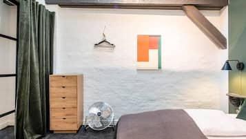 Een slaapkamer met een bed, een dressoir, een ventilator, een wandlamp en een schilderij.