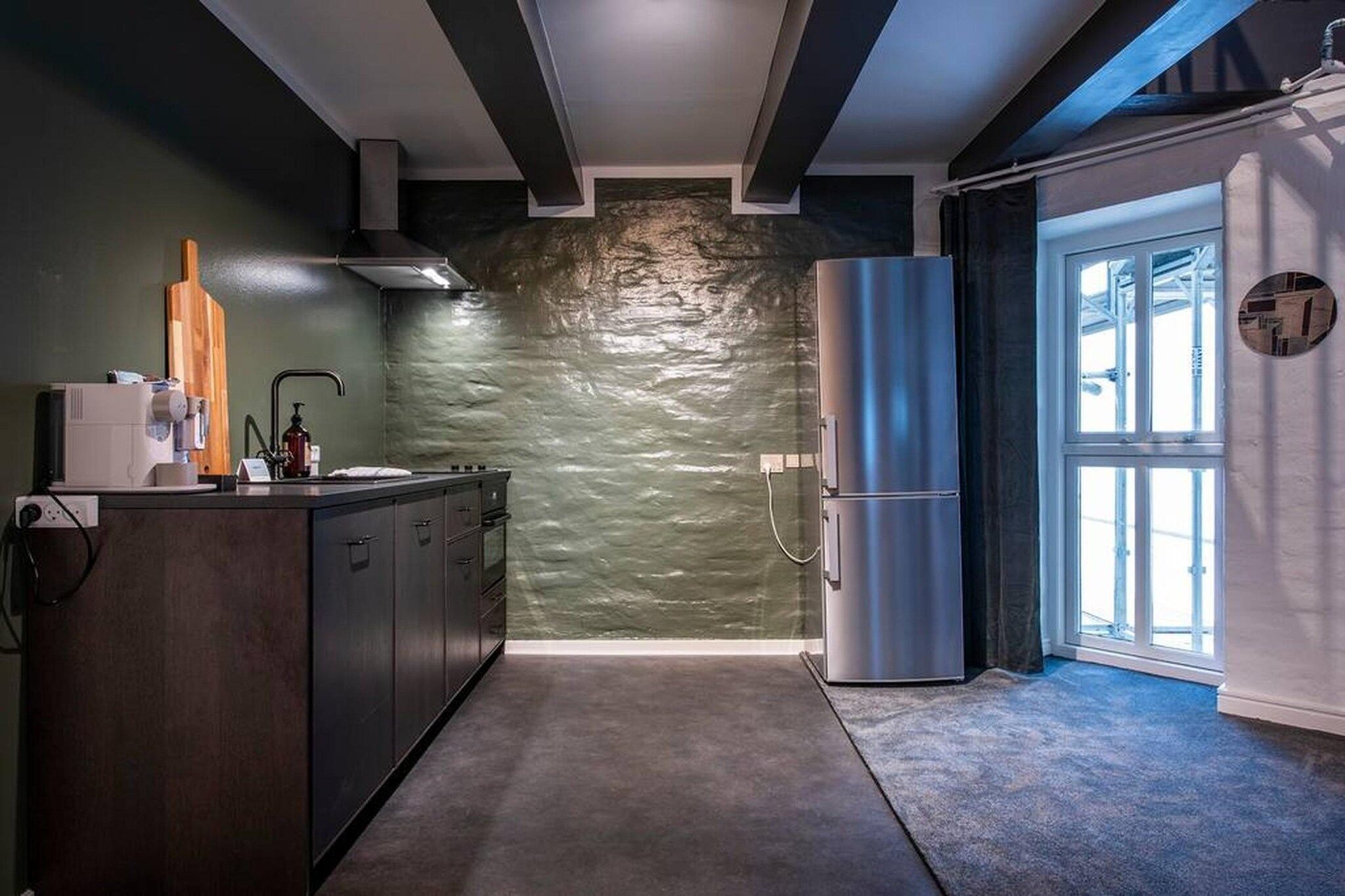 A modern kitchen with a stone backsplash, a built-in oven, and a stainless steel refrigerator.