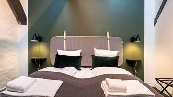 A neatly made bed with pillows and folded towels, two bedside lamps, and a headboard with a light fixture.