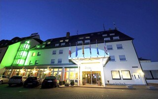 Un hotel con fachada moderna, varias banderas y una entrada bien iluminada.