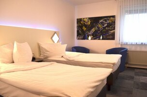 Habitación de hotel con dos camas, un escritorio, una silla y un cuadro abstracto grande en la pared.