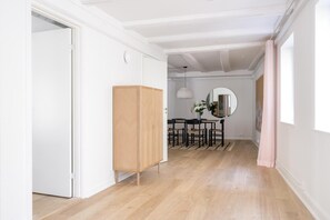 Un pasillo con un armario de madera, una zona de comedor con mesa y sillas, y un espejo grande en la pared.