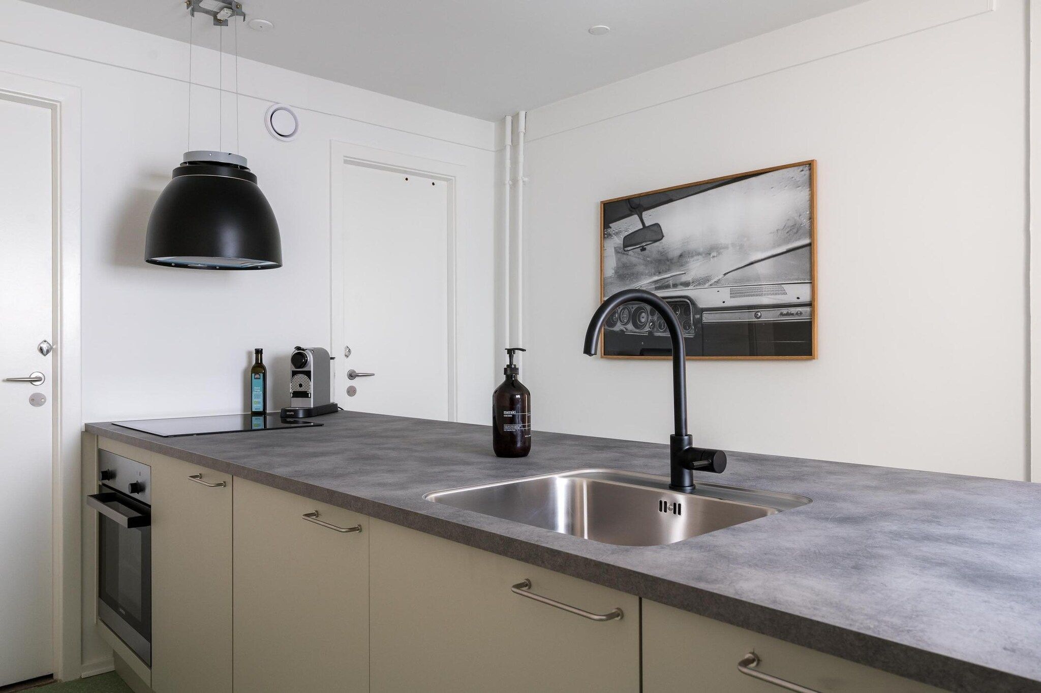Una cocina con un lavamanos doble, una lámpara colgante negra, una foto en un marco en la pared y un horno empotrado.