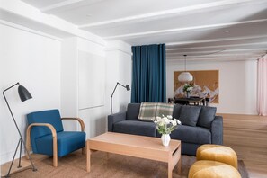 Una sala moderna con un sofá, un sillón azul, una mesa de centro de madera y un reposapiés amarillo.
