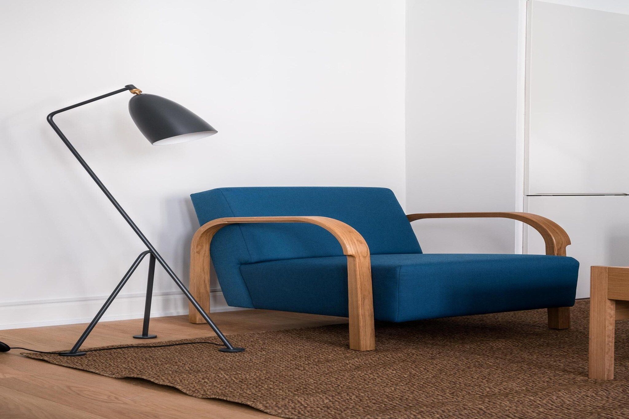 Un sillón azul con reposabrazos de madera y una lámpara de pie negra con trípode.
