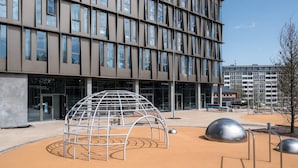En moderne bygning med et vinduesmønster og et legeområde med en kuppelformet struktur og metalskulpturer.