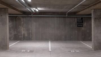 Un parking souterrain vide, avec des murs en béton, des poutres métalliques et un panneau indiquant l’emplacement de la zone de stationnement.