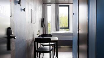 A modern room with a bed, a desk with chairs, a television, and a window with curtains.