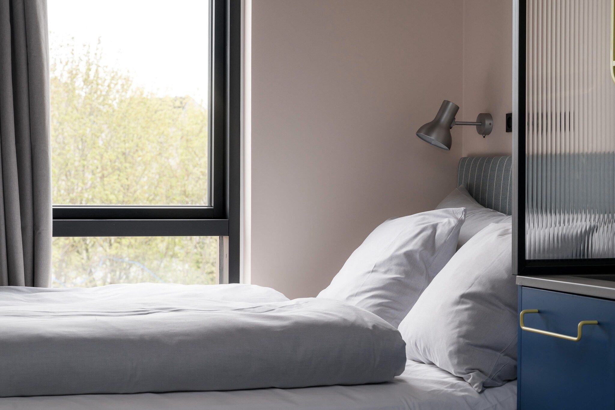 Un dormitorio con cama, lámpara de noche y ventana con cortinas.