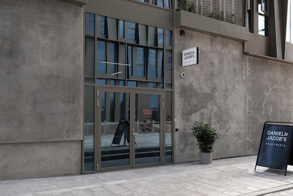 Entrada de edifício com porta de vidro, placa e planta em vaso.
