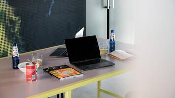 A laptop on a table with a book, a glass of beer, a bottle of water, and a can of soda.