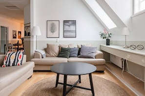A modern living room with a sofa, a round coffee table, and a dining area with a table and chairs. There are two framed pictures on the wall, a lamp, and a plant on a shelf. - Family Retreat Near Kongens Nytorv (København)