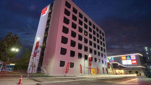 A modern hotel building with a distinctive pink facade, multiple windows, and a prominent red logo on the side. - Go Hotel Ban Chang (Ban Chang)
