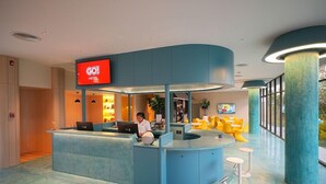 A hotel reception area with a curved blue counter, a digital display, and a seating area with yellow chairs. - Go Hotel Ban Chang (Ban Chang)