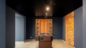 A room with a foosball table, a brick wall, and a wooden cabinet with trophies. - Edenhall Apartments & SPA (Duszniki-Zdrój)