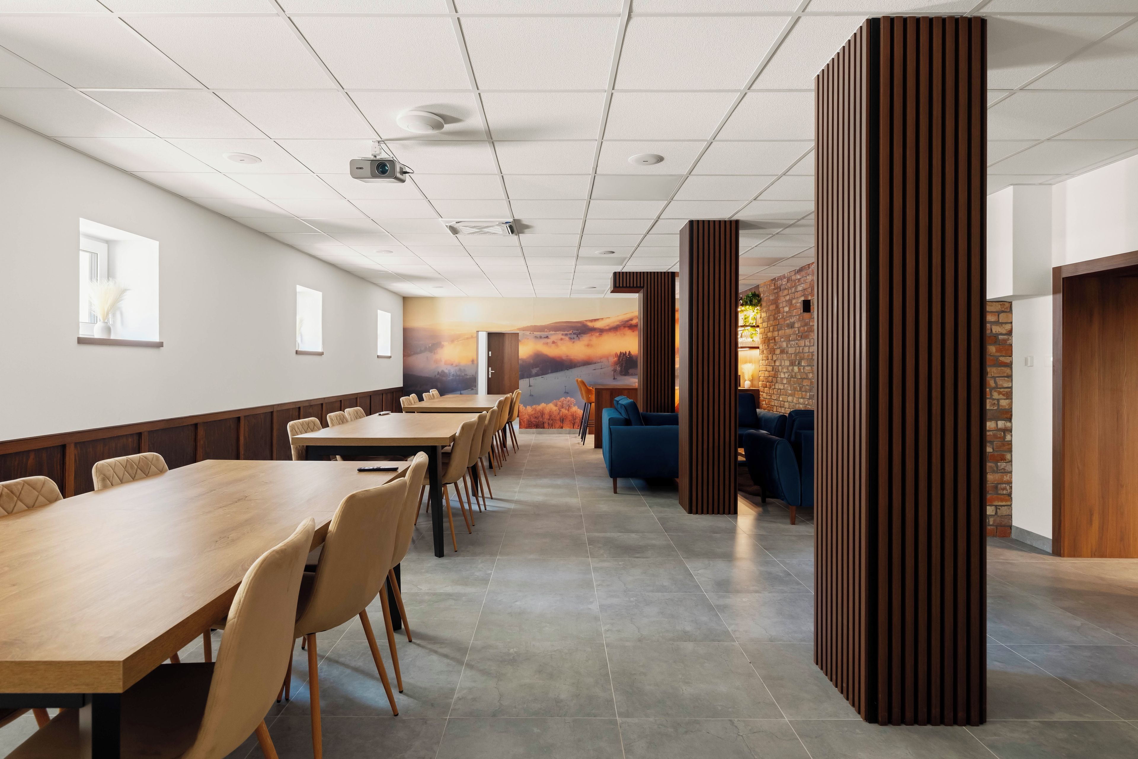 A conference room with a long table, chairs, a projector, and a mural of a sunset.