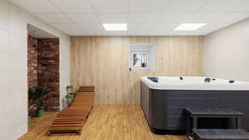 A modern bathroom with a wooden floor, a brick accent wall, a wooden bench, and a hot tub.