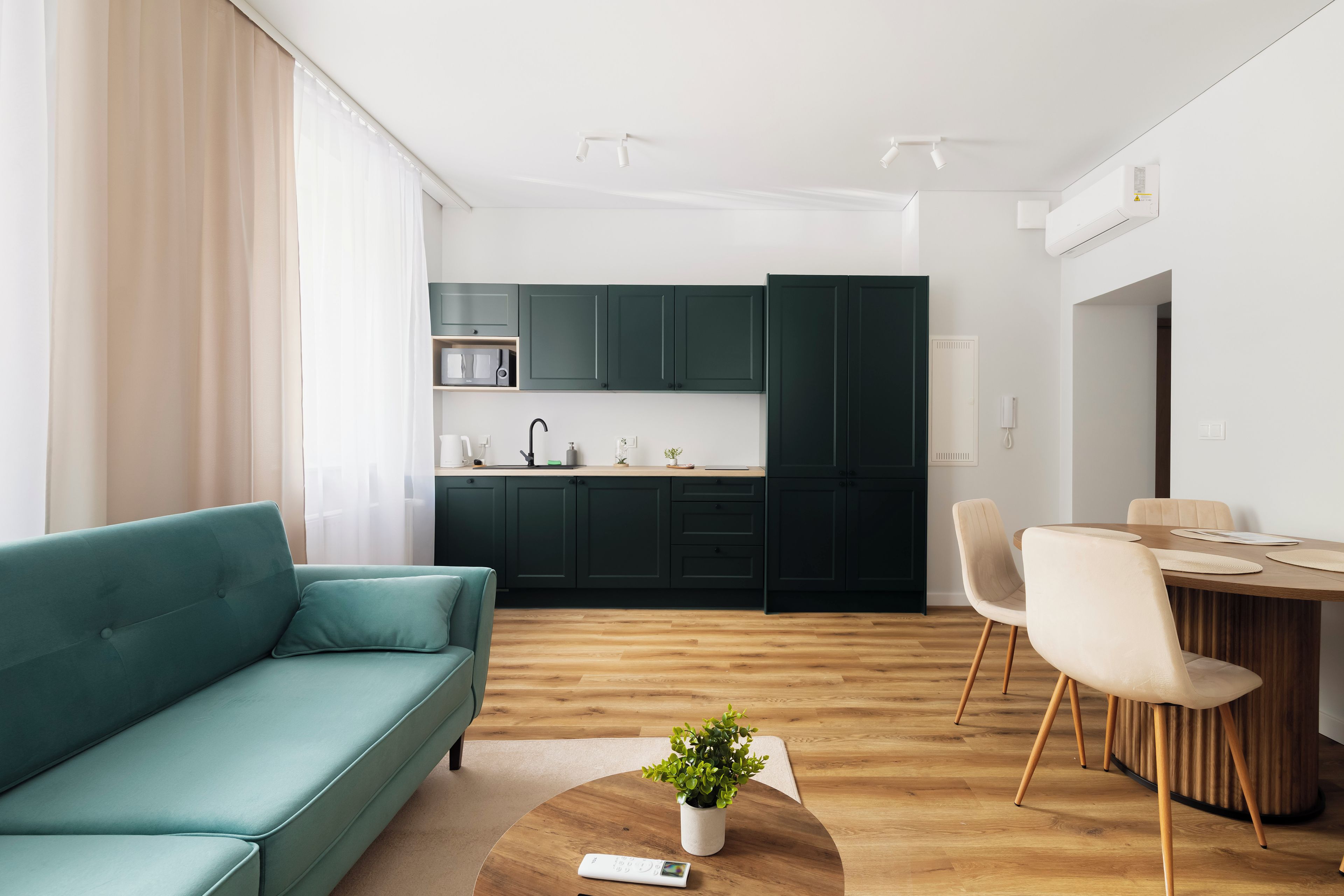 Un salon moderne avec un canapé de couleur turquoise, une table à manger en bois avec des chaises, et un coin cuisine doté de meubles de couleur vert foncé.