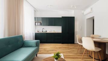 Un salon moderne avec un canapé de couleur turquoise, une table à manger en bois avec des chaises, et un coin cuisine doté de meubles de couleur vert foncé.