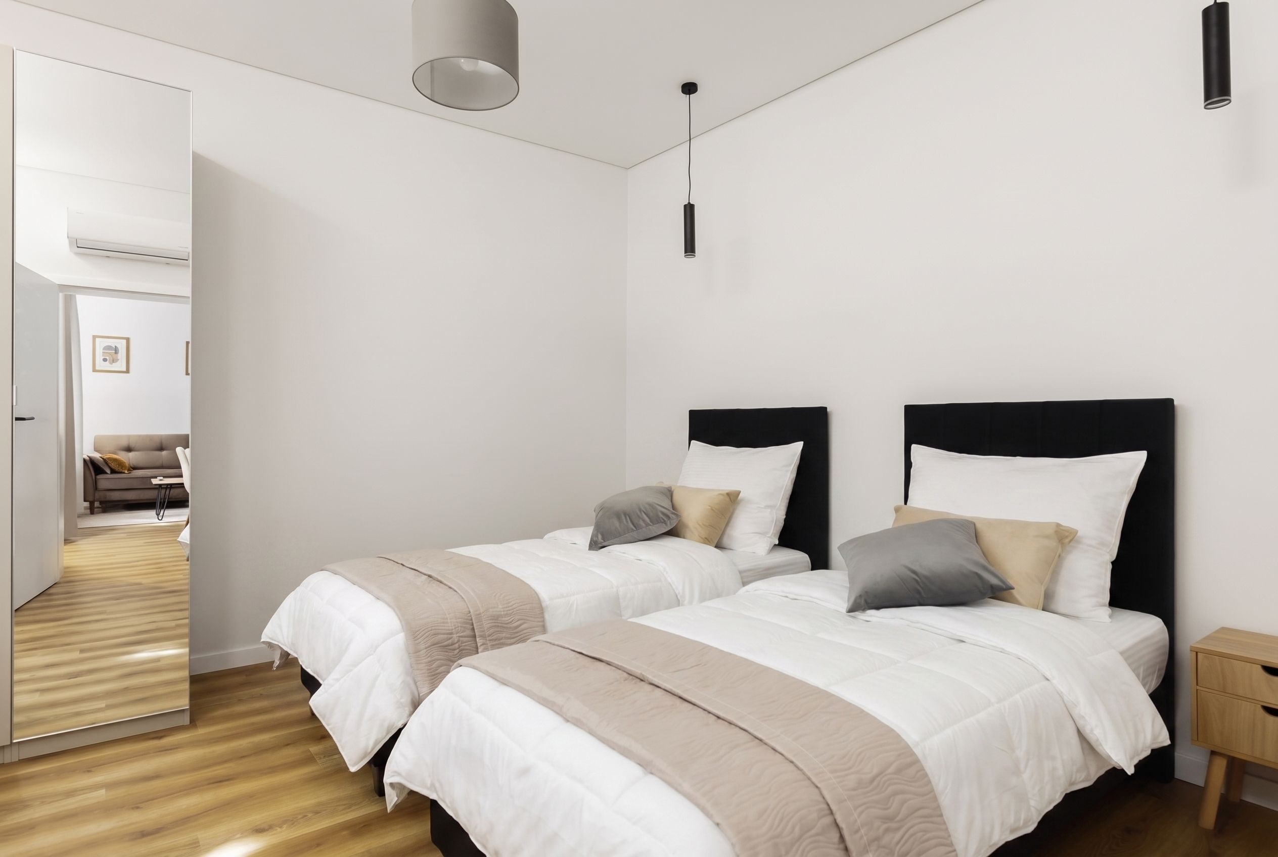 A modern bedroom with two beds, a wooden floor, and a door leading to another room.