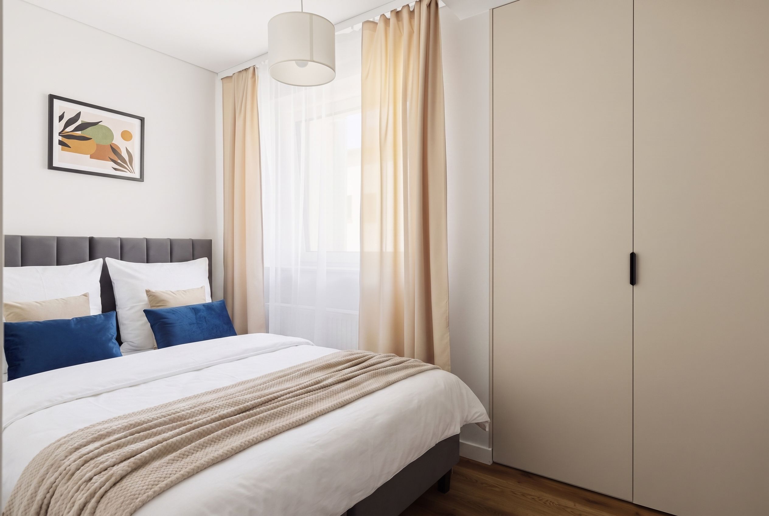 Une chambre à coucher comprenant un lit, une tête de lit, une table de chevet, une lampe, une armoire et une fenêtre avec des rideaux.