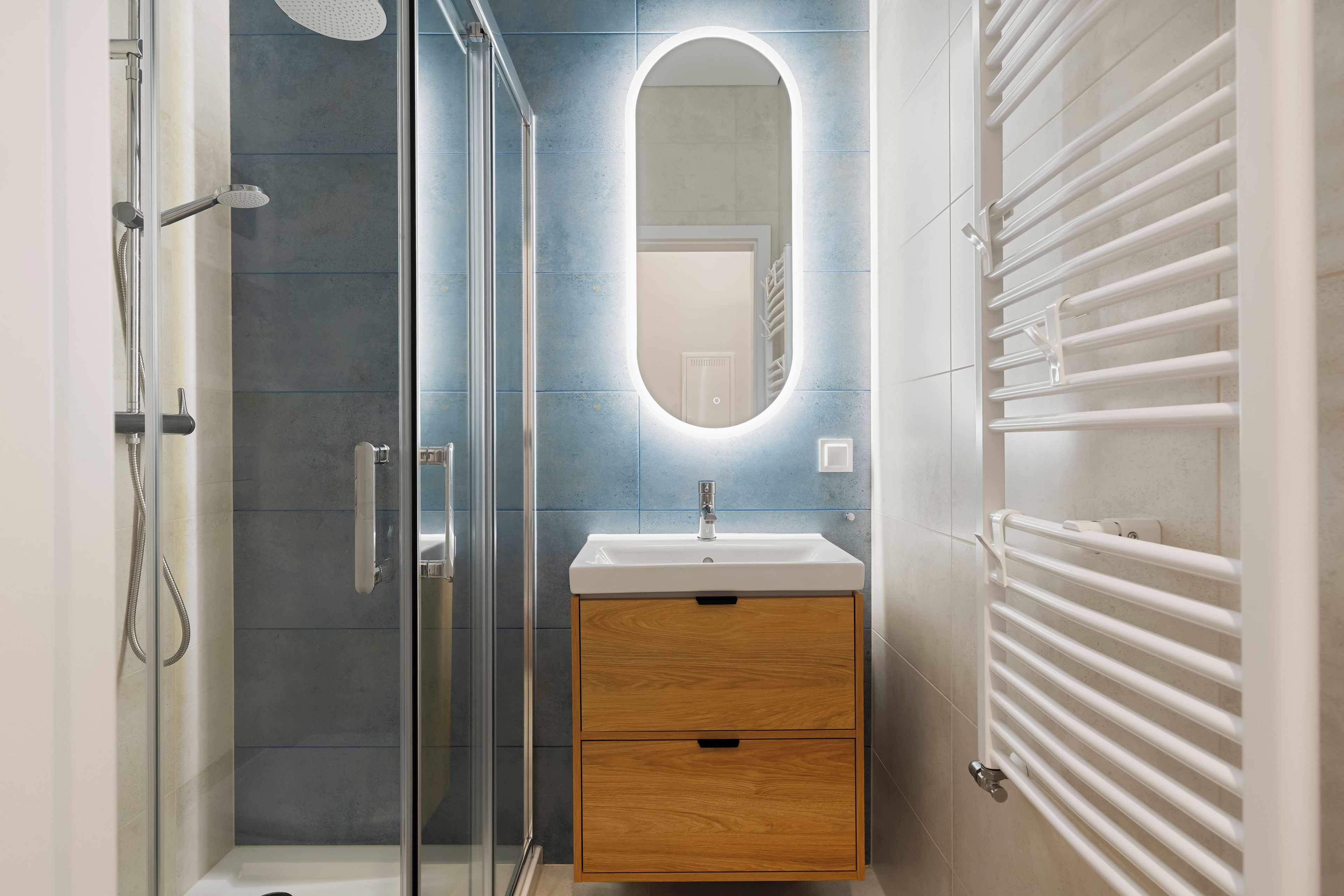 Une salle de bain moderne avec une douche à parois de verre, un meuble-lavabo en bois avec un miroir et un porte-serviettes blanc.