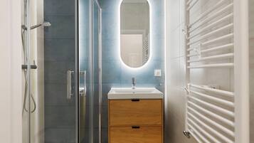 Une salle de bain moderne avec une douche à parois de verre, un meuble-lavabo en bois avec un miroir et un porte-serviettes blanc.