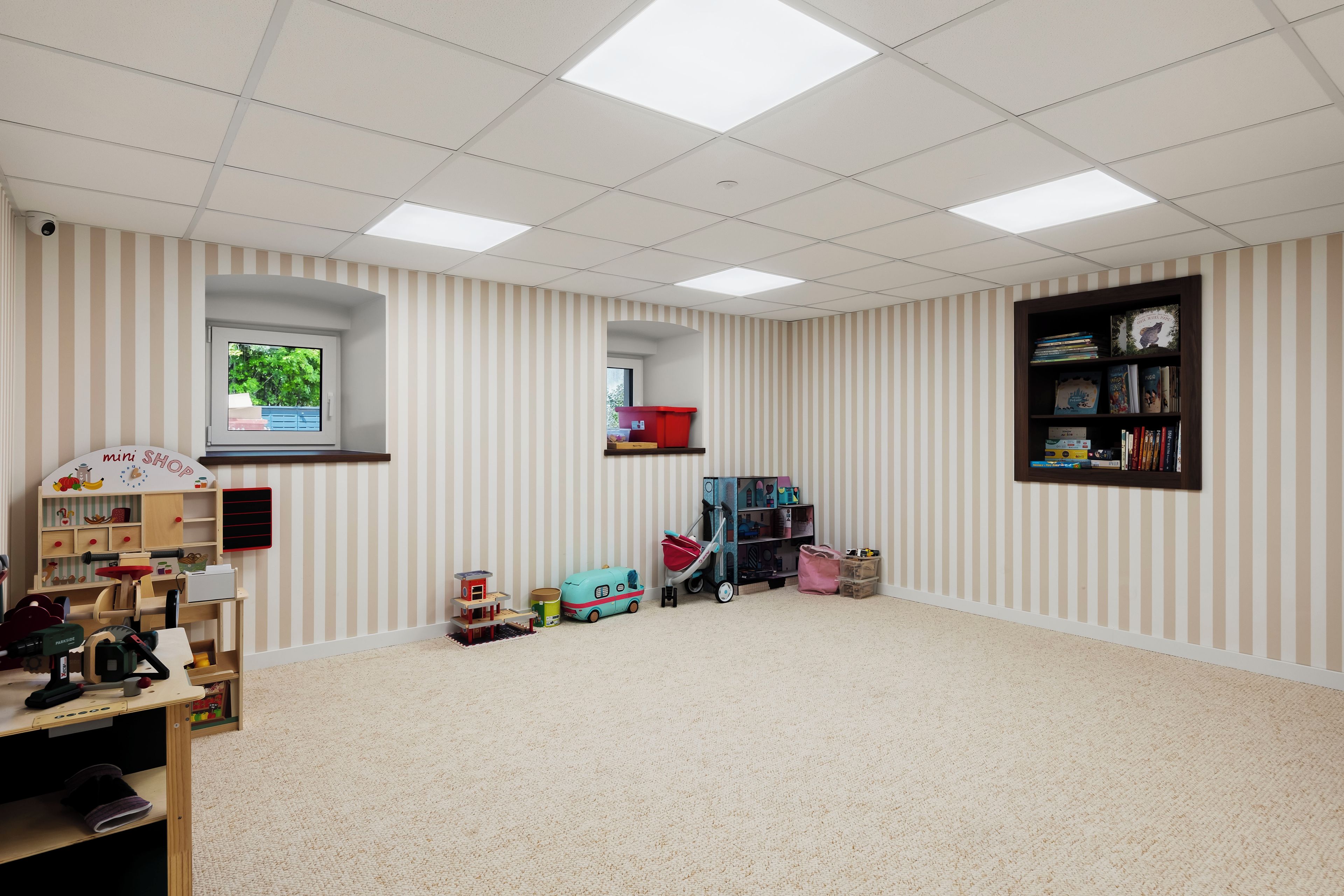 Una habitación con pared a rayas, una estantería, una ventana y una tienda de juguetes.