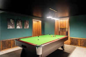 A pool table with a green felt surface, surrounded by wooden paneling and a green wall.
