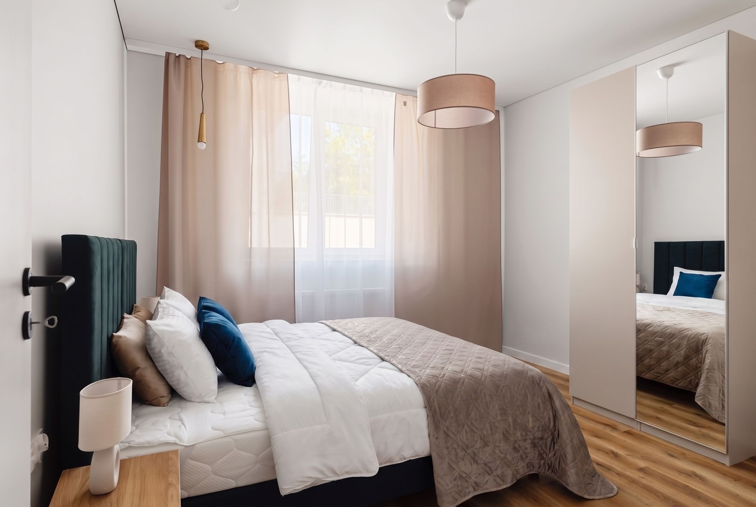 A modern bedroom with a bed, bedside table, lamp, and a large mirror.