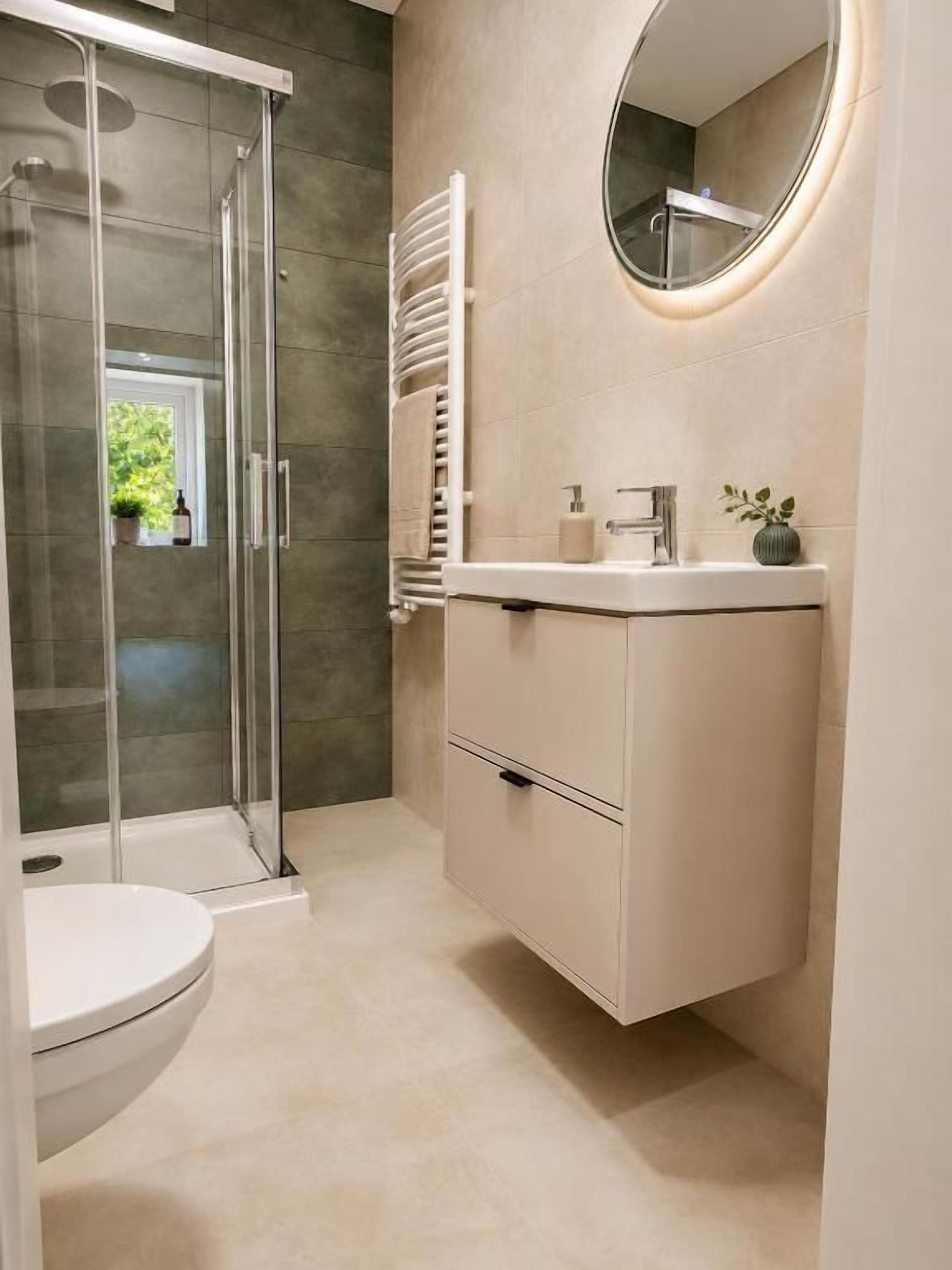 Un baño moderno con cabina de ducha de vidrio, inodoro, tocador con espejo y perchero.