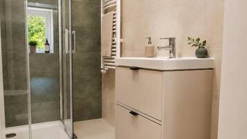 Un baño moderno con cabina de ducha de vidrio, inodoro, tocador con espejo y perchero.