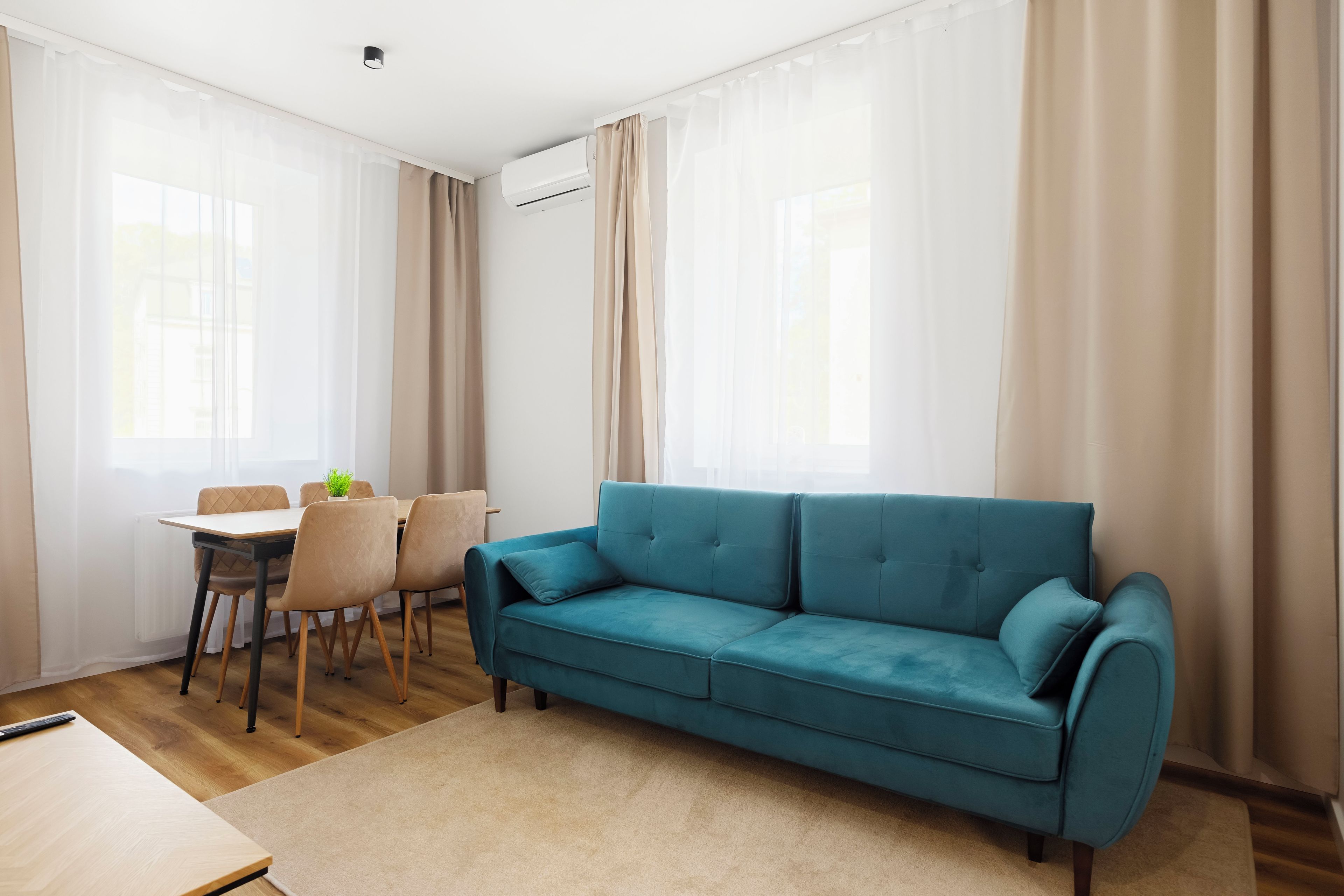 Ein modernes Wohnzimmer mit einem Türkis-farbenen Sofa, einem Esstisch mit Stühlen und transparenten Vorhängen.