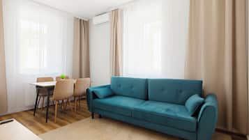 Ein modernes Wohnzimmer mit einem Türkis-farbenen Sofa, einem Esstisch mit Stühlen und transparenten Vorhängen.