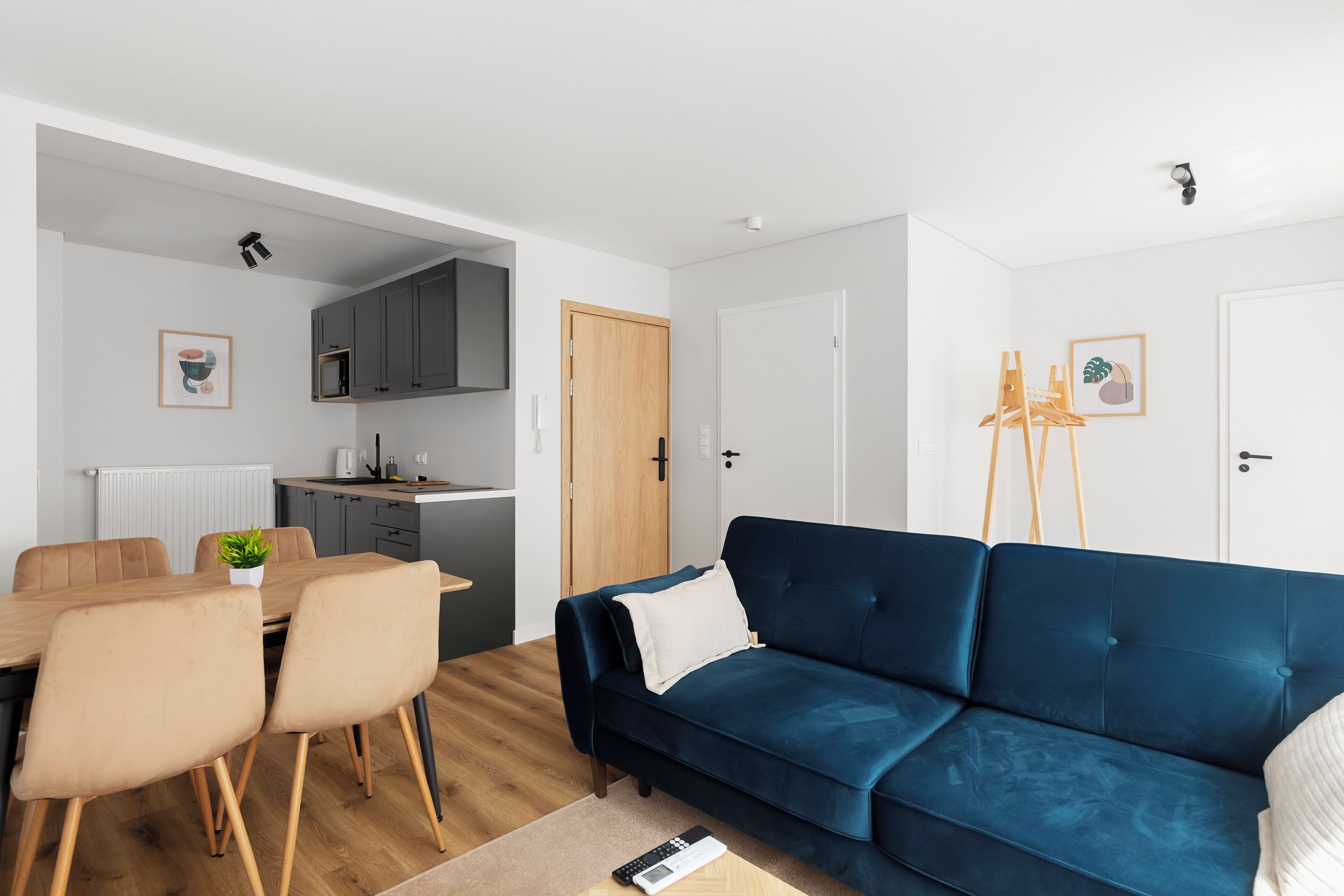 Een moderne woonkamer met een donkerblauwe bank, een eethoek met een houten tafel en stoelen, en een keuken met grijze kastjes.