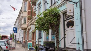 Une rangée de bâtiments avec un café au rez-de-chaussée, des tables à l’extérieur et un panneau indiquant un parking.