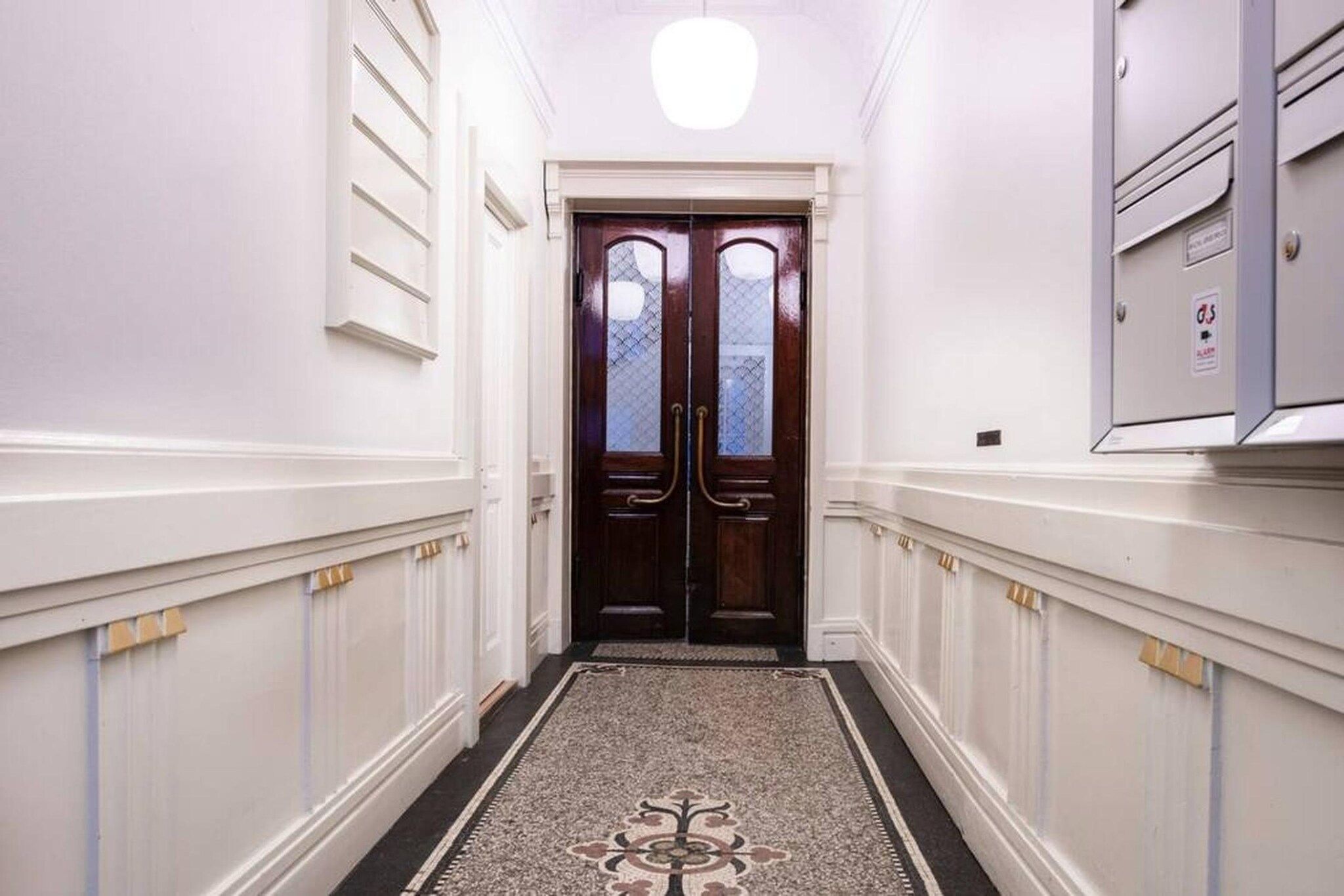 A hallway with a double door, white walls, and a patterned rug.