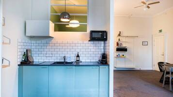 A kitchen with a blue countertop, white tiles, a microwave, and a hanging pendant light.