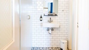 Une salle de bain avec des carreaux de céramique blancs rectangulaires, un lavabo blanc, un miroir, un porte-serviettes et des toilettes.