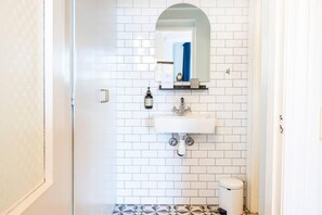 Casa de banho com azulejos brancos tipo metrô, pia branca, espelho, porta-toalhas e sanita.