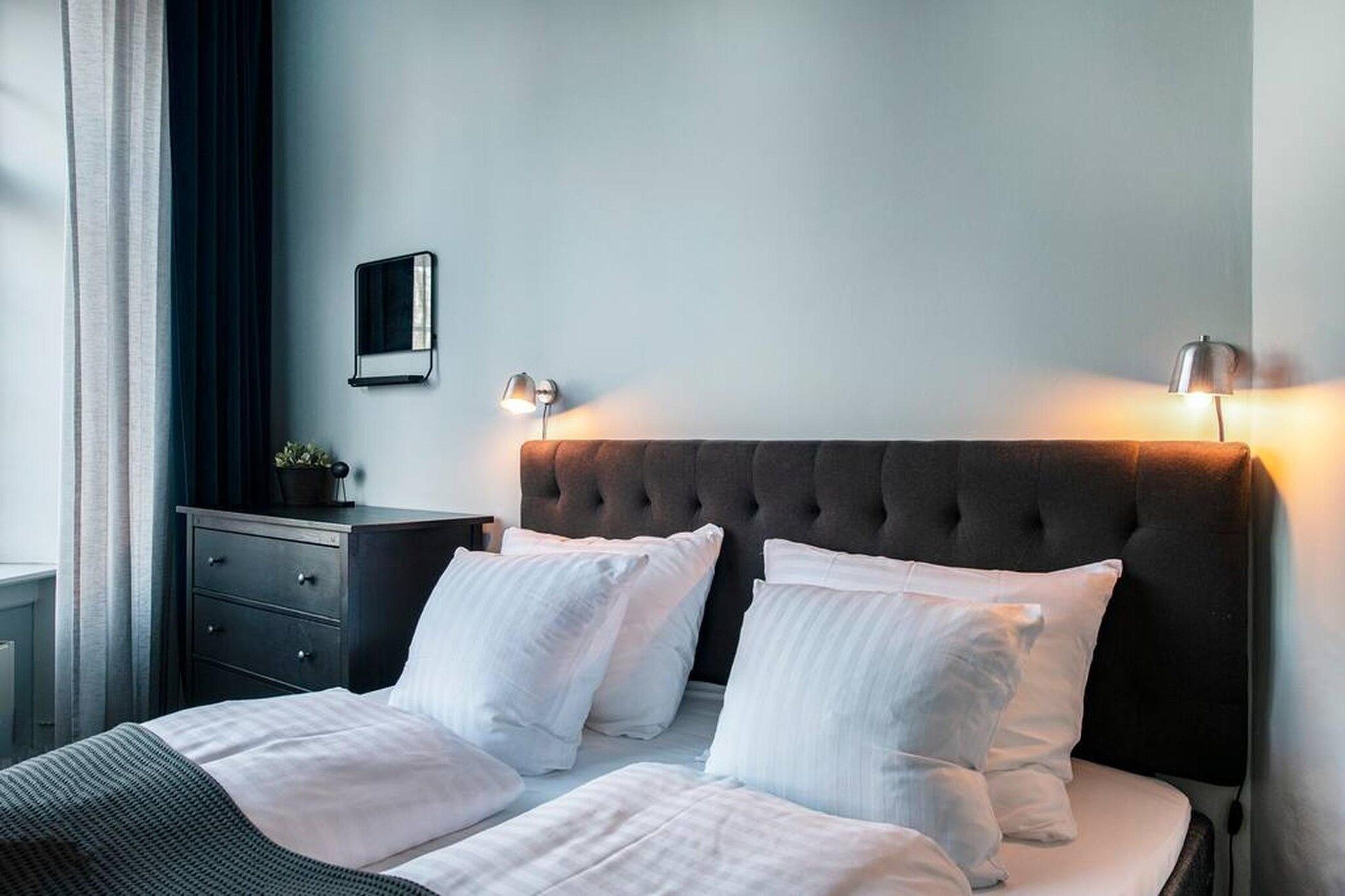 A hotel room with a large bed, two bedside tables, a dresser, and a wall-mounted mirror.